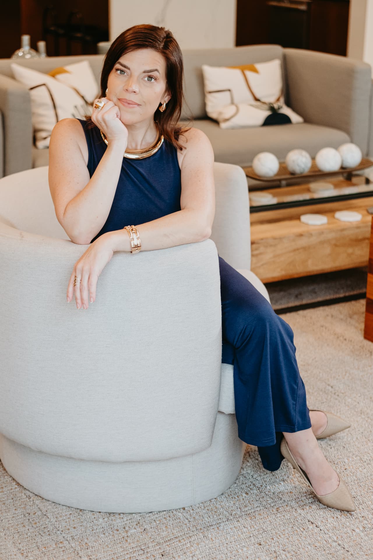 Kellena in a navy dress seated in an ivory chair, chin resting on her hand